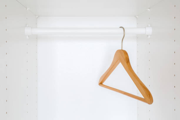 Wooden empty hanger without clothes on rail into white wardrobe at home. Closeup. Front view.