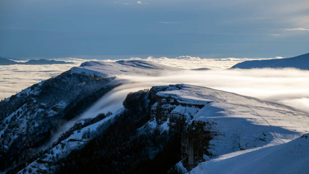 A desolate winter mountain landscape with frosted plants in the foreground and sunlight through overcast clouds in the background