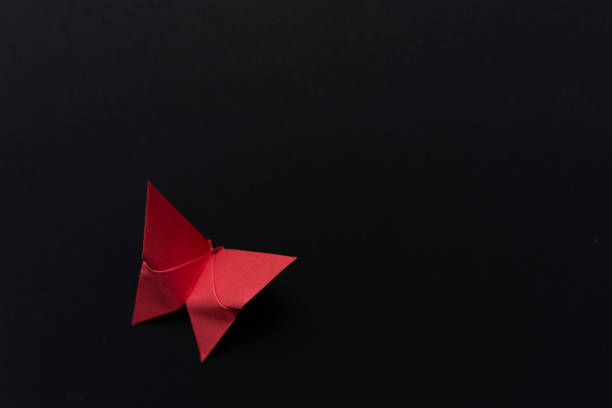 A beautifully crafted red paper butterfly resting on a dark surface, creating a striking contrast. Ideal for greeting cards, posters, and artistic compositions.