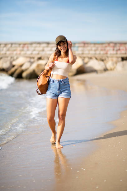 istock Attractive young woman walking on the beach with bag 2197588939
