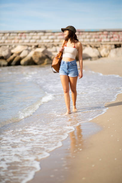 istock Beautiful young woman walking on the beach with bag 2197588972