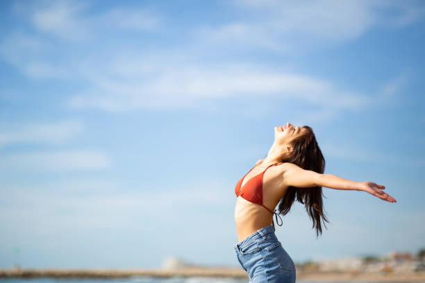istock Happy young woman standing on beach with hands outstretched 2197589042