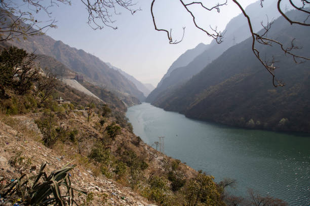 A tranquil river flows gracefully between tall, picturesque mountains under a clear, bright sky. The natural landscape is surrounded by serene beauty, featuring untouched wilderness and evoking peace and adventure.