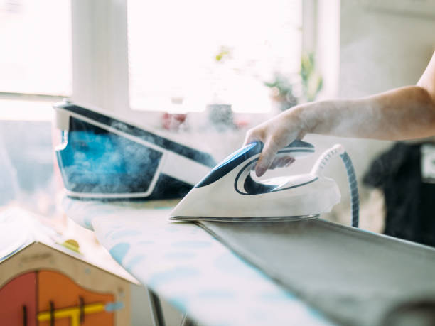 istock Person Ironing Clothes with a Modern Steam Iron in a Bright Room 2197593096