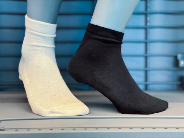 A mannequin foot displays a pair of contrasting socks—one white and one black—against a modern retail background, highlighting textile design and fashion choices.