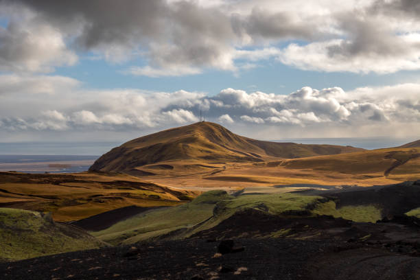 Volcanic rocks and mountains having a velvet surface in the autumn, thanks to the yellow moss, lichen and grass. Atlantic ocean in the background. Blue sky with white clouds. Katla geopark, Iceland.