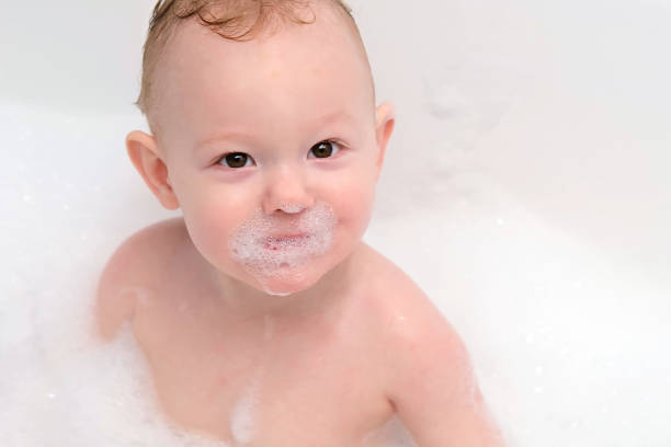 Close up of child’s face surrounded with bubble foam lying in a bathtub , having his daily washing routine