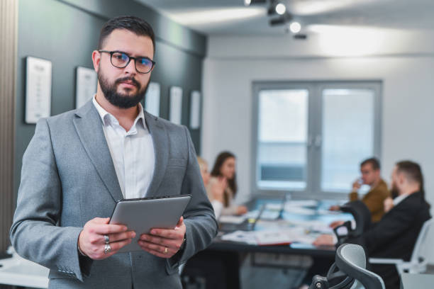 istock Male Supervisor Looking at Camera With Serious Facial Expression Holding Digital Tablet 2197600507
