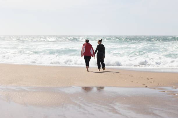 istock Two friends women Walking on a Beach Holding Hands 2197600609