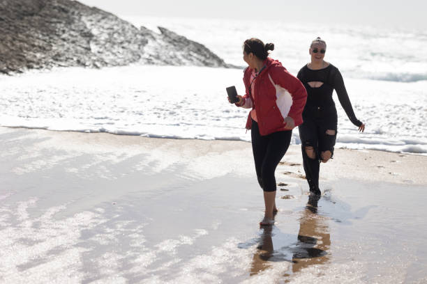 istock Two Women Walking Along Beach Next to Ocean 2197600705