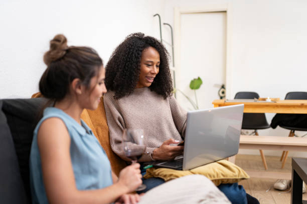 istock Female friends drinking wine and using laptop at home 2197603913