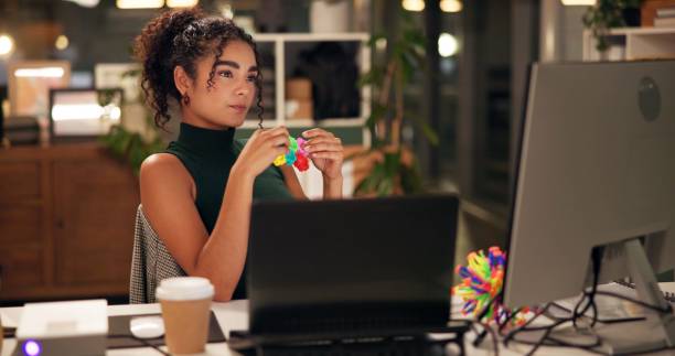 istock Business woman, computer and thinking with popit toy, creative agency and ideas for night brainstorming. Girl, brand consultant or multi screen laptop with project, proposal or office fidget stimming 2197604077