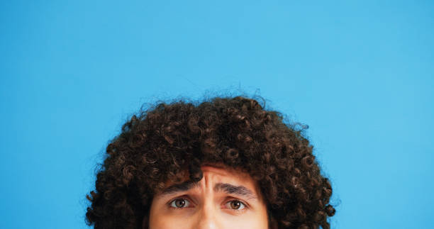 istock Raised eyebrow, confused or man in studio portrait with puzzled expression, emoji or eyes. Curly, unsure or afro hair guy with doubt, question or worry on blue background mockup for styling product 2197604718