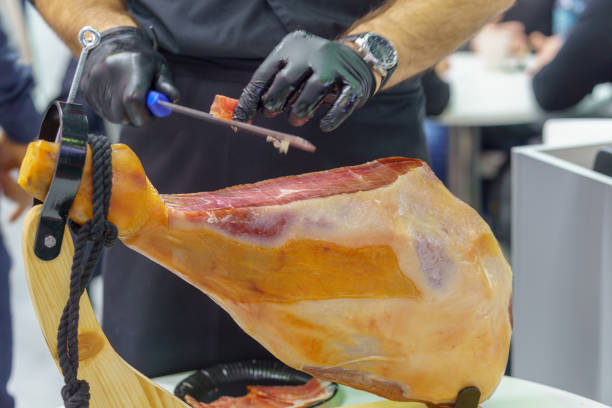 A man is cutting a piece of meat with a knife. The meat is a large piece of ham