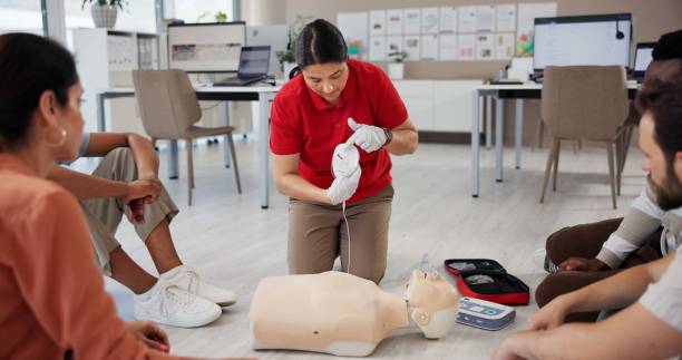 istock Mannequin, first aid and class with people and defibrillator for workshop, cardiac arrest and safety protocol. Healthcare, medical simulation and heart rhythm rescue with paramedic course in office 2197609568