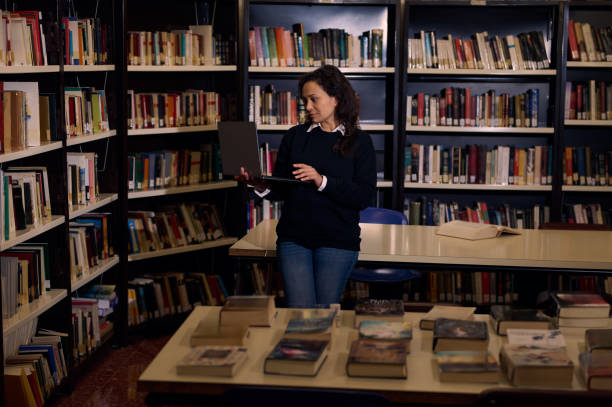istock Woman Using Laptop in Library Surrounded by Bookshelves and Tables 2197609614