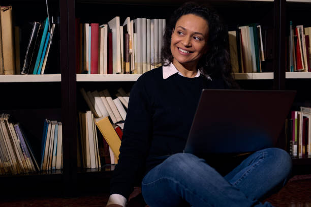 istock Smiling woman with a laptop in a cozy library setting 2197609634