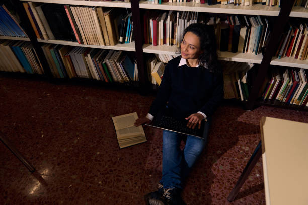 Woman studying with a laptop and book in a library for knowledge