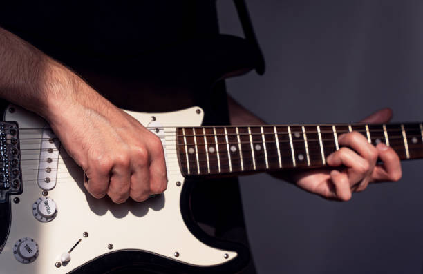 istock a man playing an electric guitar, right hand with fingers curled in focus above the strings 2197610654