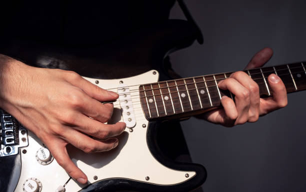 istock a man playing an electric guitar, right hand with a pick in focus above the strings 2197610661