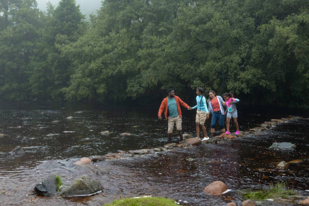 istock Parents And Kids Holding Hands While Crossing A River 2197613246
