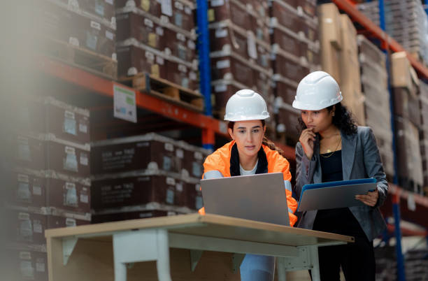 Teamwork in warehouse operations—Warehouse Manager and colleagues discussing FIFO stock arrangement on computer. Efficient supply chain planning, freight transportation, manufacturing logistics, and quality control in an industrial distribution facility
