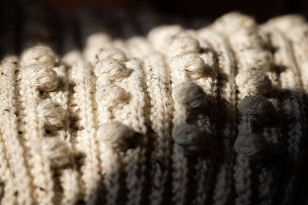 Detailed view of a cream-colored knitted fabric featuring intricate patterns, captured under warm, soft lighting.