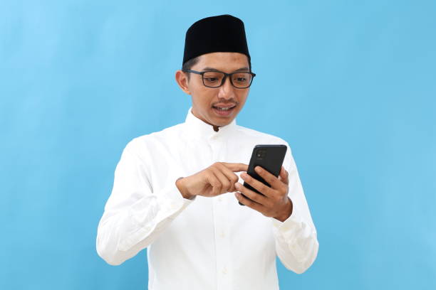 istock Portrait of asian muslim man standing while using cell phone. Isolated on blue 2197619778