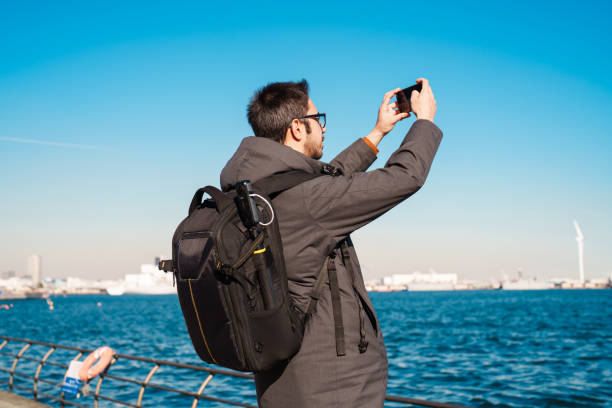 A man is taking photos with his mobile phone by the sea.