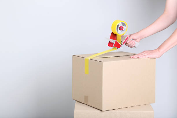 istock Female hands packaging cardboard box with dispenser on grey background 2197623883