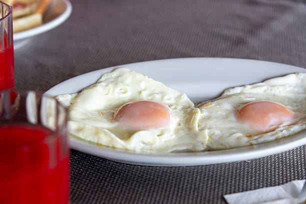 A couple of fried eggs on white plate red fruit juice on glasses