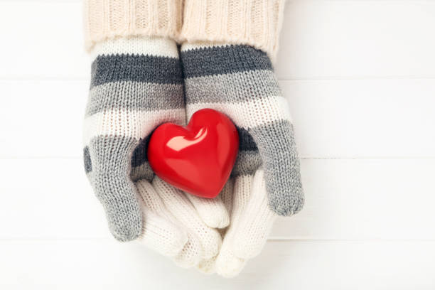 istock Hands in knitted mittens holding heart on white wooden table 2197626887