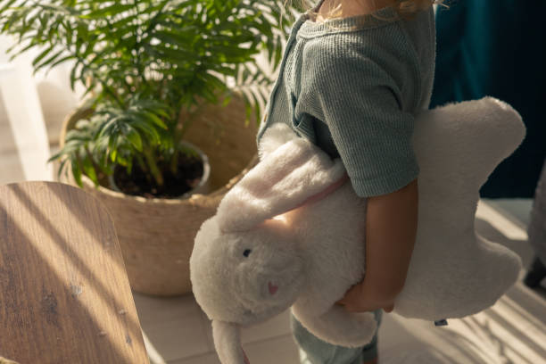 A child enjoys Easter festivities by holding a soft bunny toy. The cozy atmosphere features plants and warm sunlight, symbolizing the joy of spring and holiday traditions.