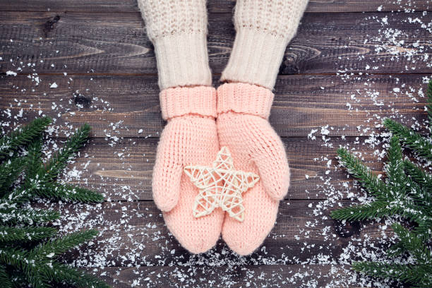 istock Hands in knitted mittens holding star and fir tree branches on wooden table 2197627480