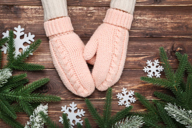 istock Hands in knitted mittens with snowflakes and fir tree branches on wooden table 2197628069