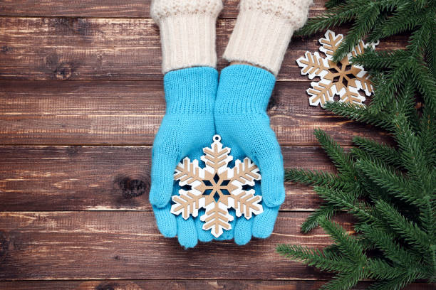 istock Hands in knitted mittens holding snowflake and fir tree branches on wooden table 2197628577