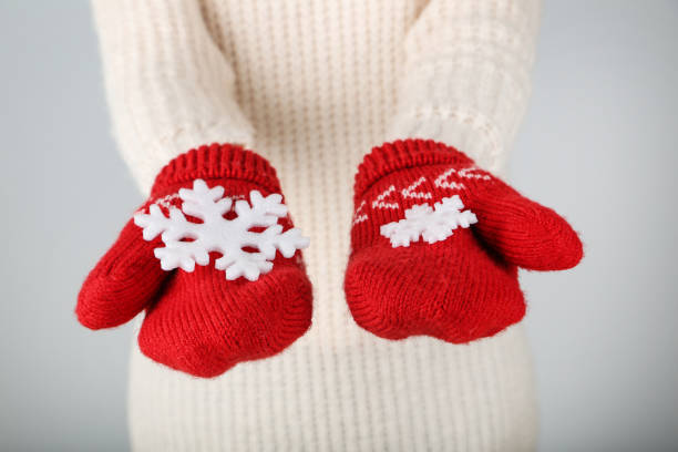 istock Hands in knitted mittens holding snowflakes on grey background 2197629364