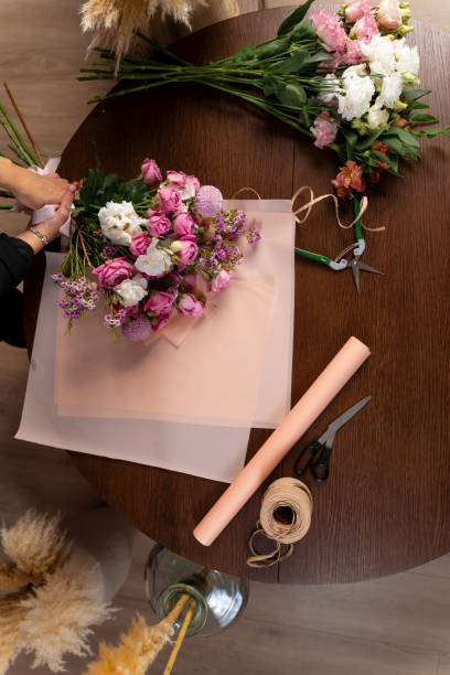istock Florist makes a composition of flowers from roses and carnations for the client. Wrapping a bouquet from mixed flowers in pack paper by florist in floral shop. 2197631454