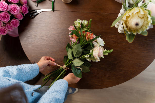 istock Florist making bouquet of bloom flowers at studio. Preparing fresh flowers before making blooms composition. Female florist is holding and designing a bouquet composition. 2197631805