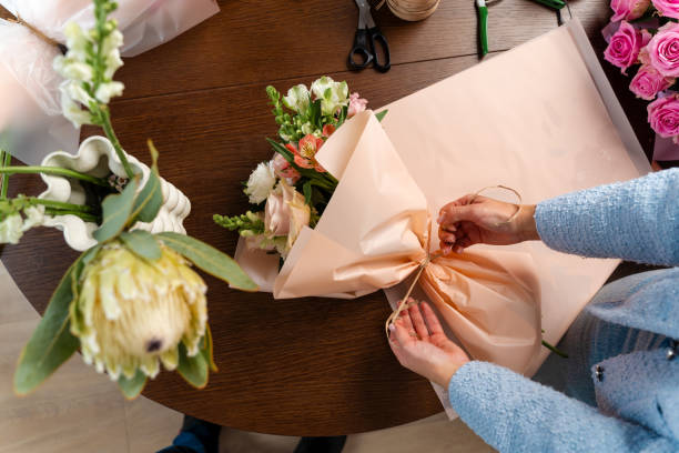 istock Wrapping bouquet composition into craft paper with beautiful fresh flowers. Creating a bouquet of mixed flowers by florist in floristry salon. 2197631968
