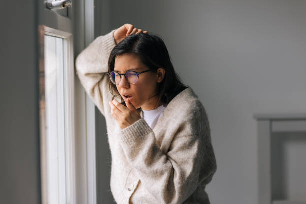 istock Woman coughing next to window 2197632798