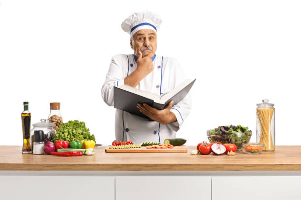 istock Confused male chef holding a cook book behind a counter 2197634112
