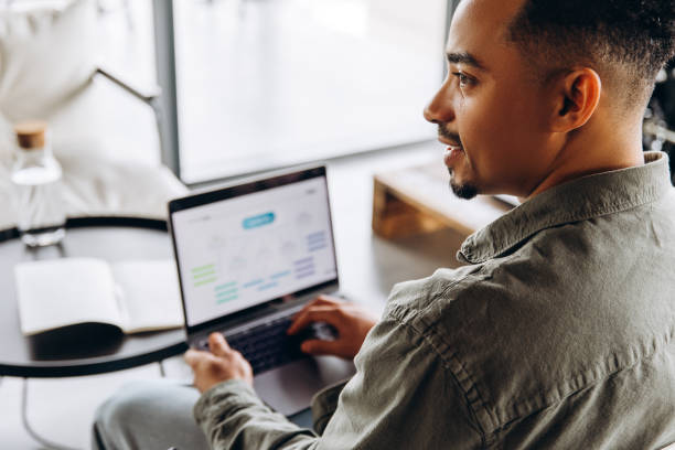 istock Young businessman working from home using laptop and smiling, over the shoulder view 2197634161