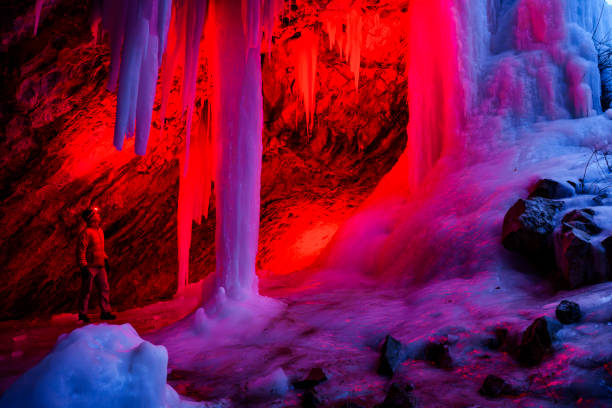 Ice Cave at Dusk - Outdoor adventure exploration in scenic outdoor area in winter with frozen waterfalls and ice caves that form behind the frozen waterfalls. Creatively lit with red light and natural blue hour cool blue light in contrast.