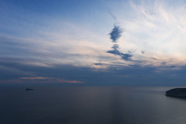 Seascape featuring a lone ship on the horizon under a twilight sky.