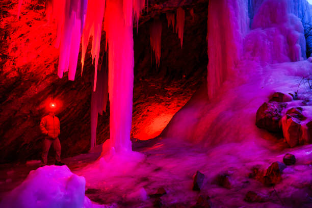 Ice Cave at Dusk - Outdoor adventure exploration in scenic outdoor area in winter with frozen waterfalls and ice caves that form behind the frozen waterfalls. Creatively lit with red light and natural blue hour cool blue light in contrast.