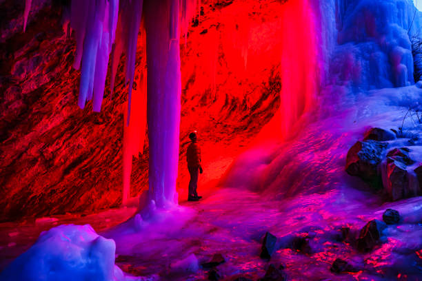 Ice Cave at Dusk - Outdoor adventure exploration in scenic outdoor area in winter with frozen waterfalls and ice caves that form behind the frozen waterfalls. Creatively lit with red light and natural blue hour cool blue light in contrast.