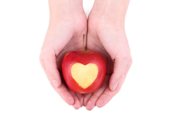 Female hands holding red apple with cutout heart shape on white background