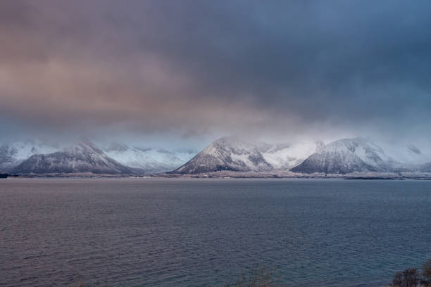 Snow-covered landscape. Mountains and a water of a Kvaerfjord. Colorful cloudy sky during sunrise/sunset. Harstad, Norway.