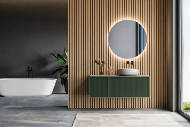 istock Modern bathroom interior with a freestanding bathtub, wooden slatted wall, round backlit mirror, and green floating vanity near a large window. 3D rendering. 2197640400